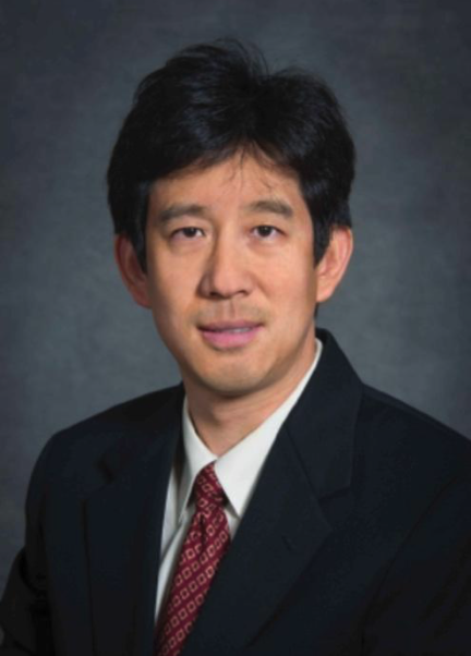 man in dark suit with a red tie and dark hair smiling